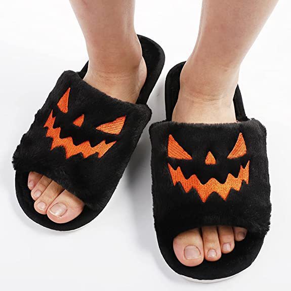 Feet wearing black plush Halloween slippers with an orange pumpkin face